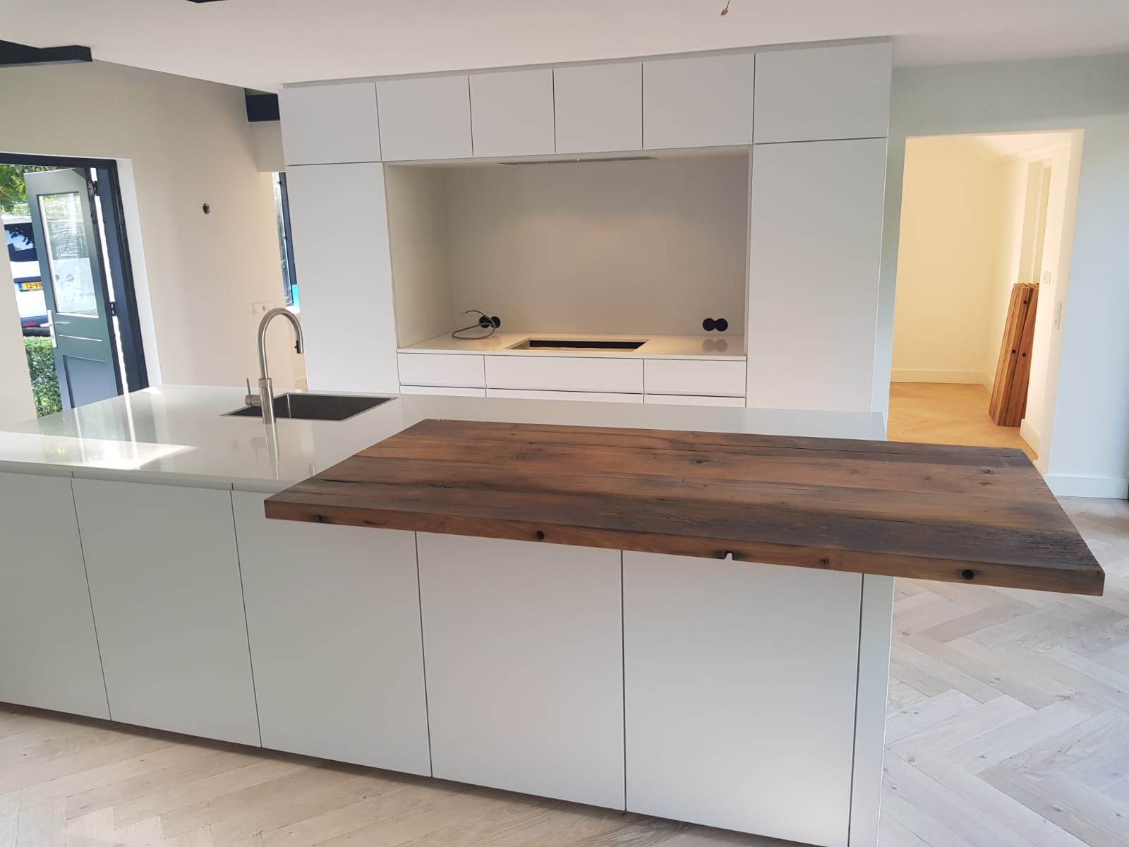 Witte greeploze keuken met lang kookeiland en een dik blad van donker hout dat over het eiland uitsteekt